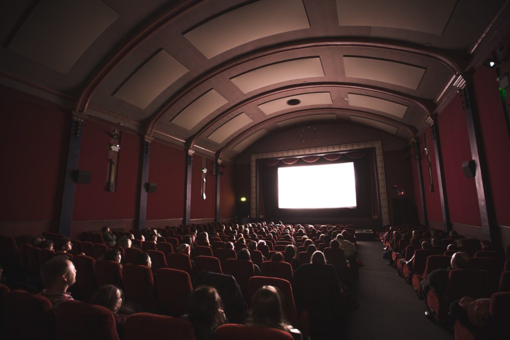 A crowd of people sit in a dark cinema watching a film.