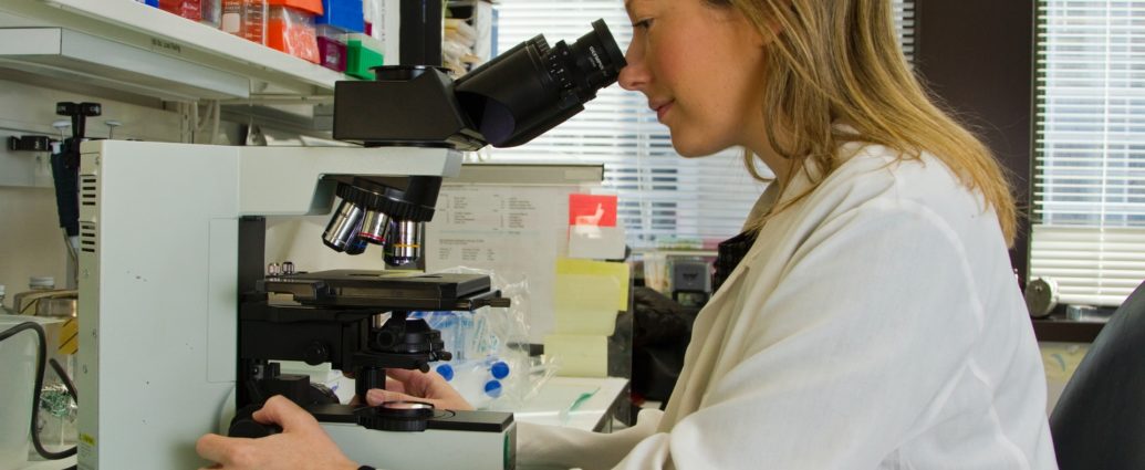 Female cancer researcher looking at a sample under a microscope