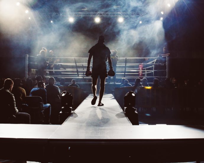 Man walking towards a boxing ring surrounded by crowd