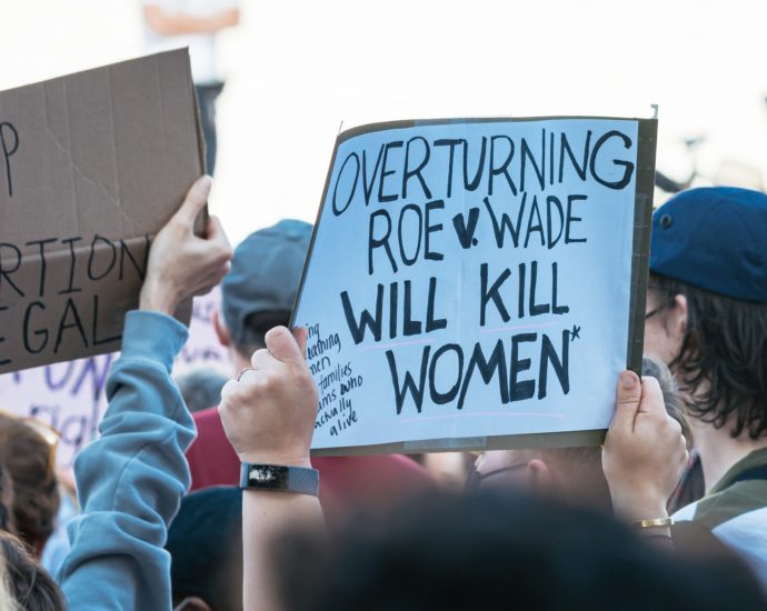 White sign with black writing held at a protest saying "overturning Roe v Wade will kill women" and another one saying keep abortion legal