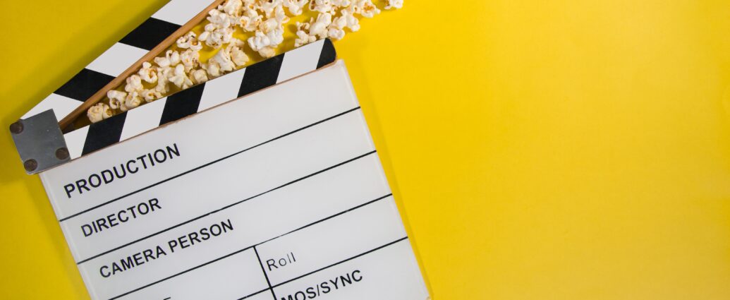 A blank movie clapperboard rests on a bright yellow background with popcorn spilled on top.