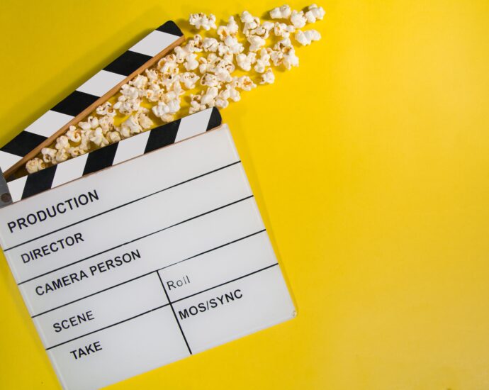 A blank movie clapperboard rests on a bright yellow background with popcorn spilled on top.