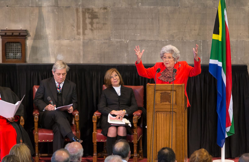 Baroness Betty Boothroyd wearing a red suit, standing behind a podium with arms raised.