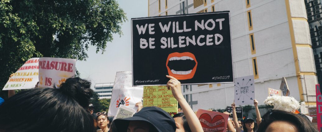 Image of a somebody holding up a sign at a women's rights protest saying "we will not be silenced"