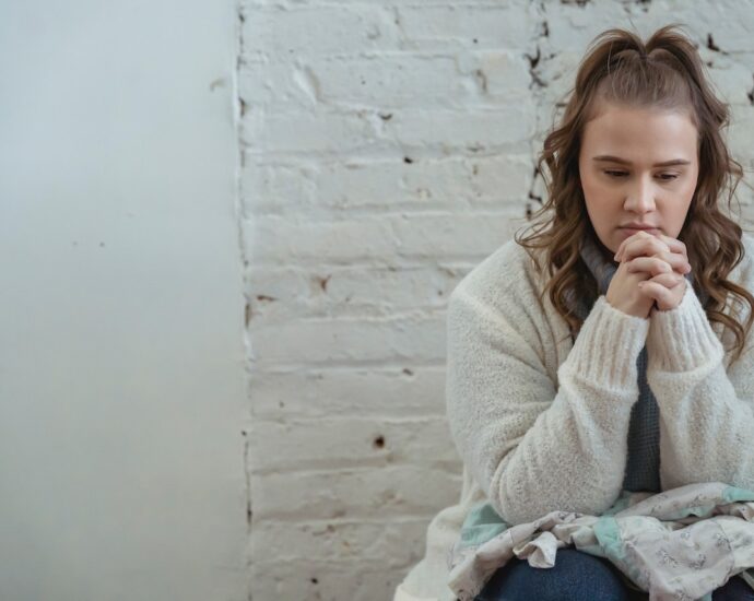 Upset woman wearing white cardigan with fingers clasped, thinking about next steps