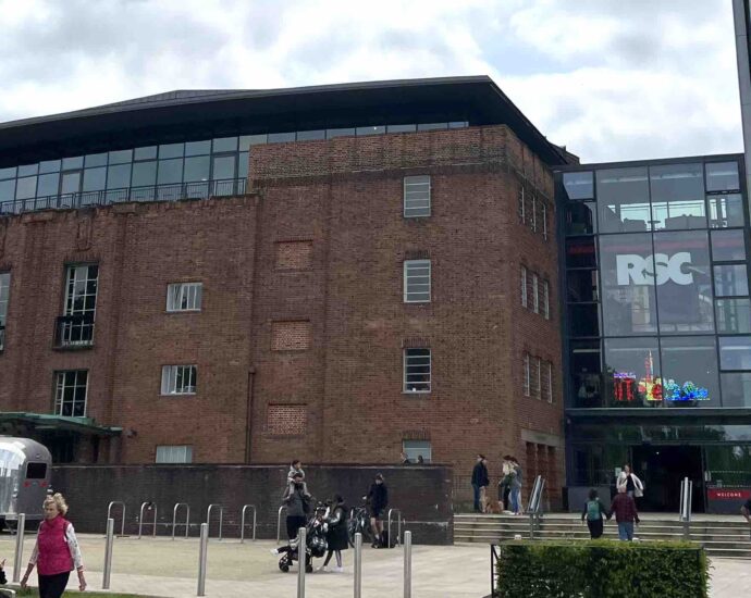 Entrance to a theatre in daylight with a tower to the right and a few people passing by