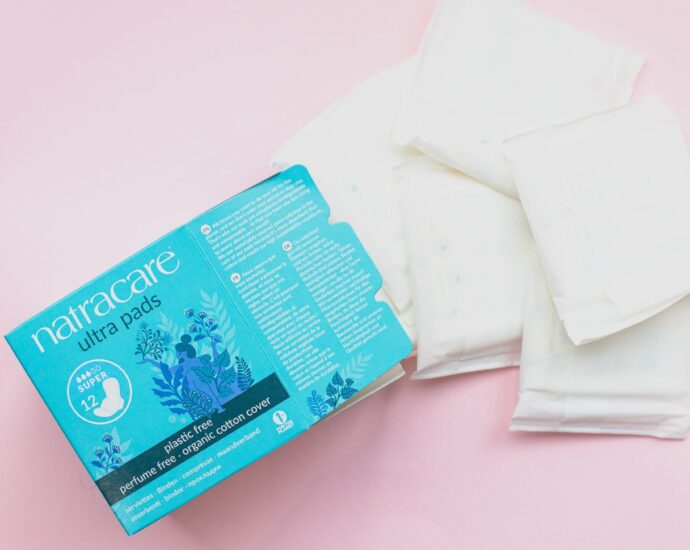 A box of period pads and some pads on a pink background