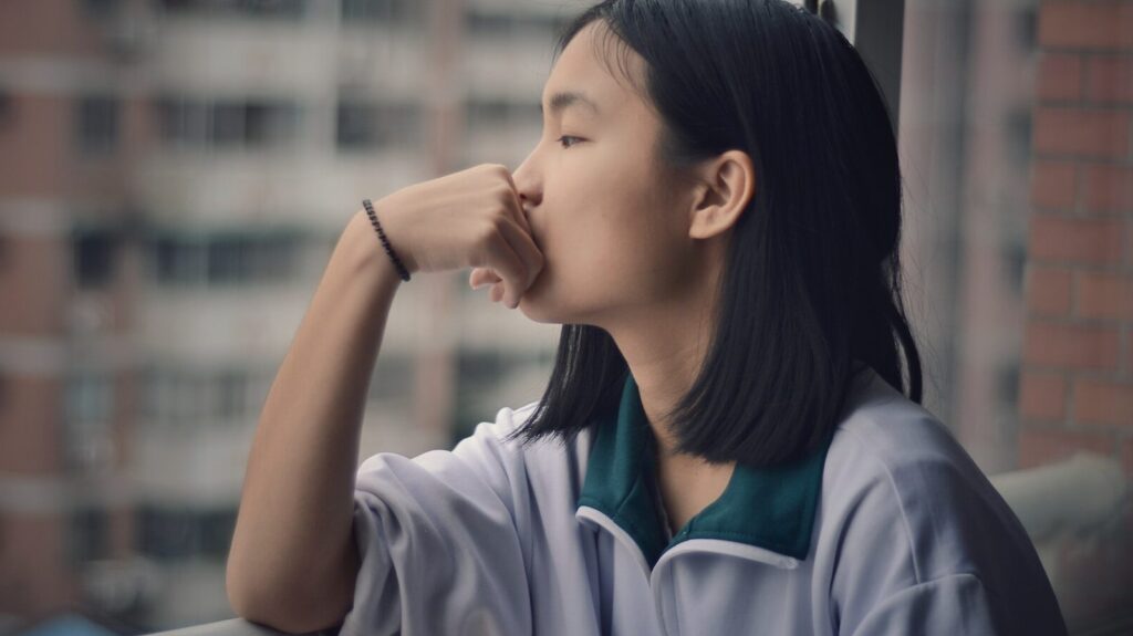 girl leaning on hand, staring out of window and overthinking