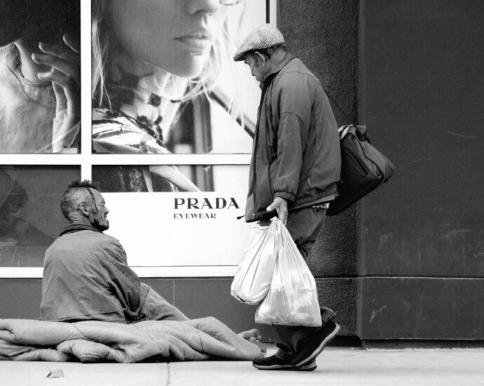 A homeless man sitting outside a Prada fashion store.