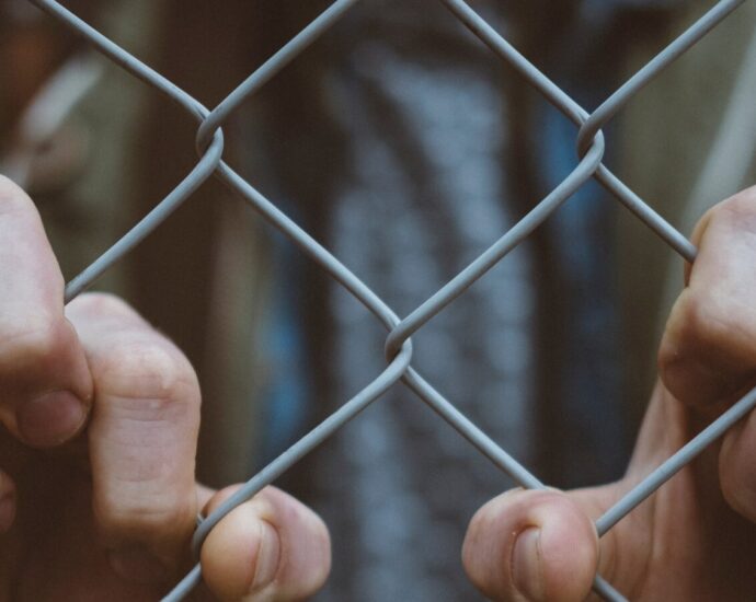Some hands gripping a barbed wire fence, reflecting how trapped the process of migration can make somebody feel.