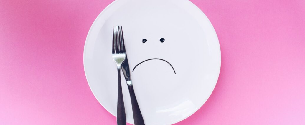 A plate with a sad face drawn on it, with a knife and fork, on a pink background.