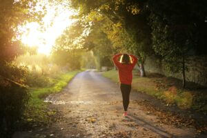 Woman with a red hoodie running along wooded path.