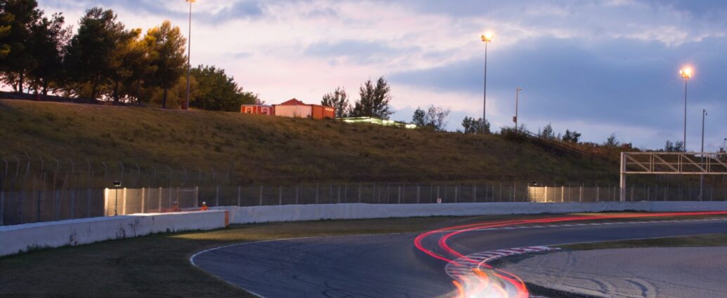 racing track at twilight, as the lights start to come on. a red blur is seen to show a car speeding past. formula one strategy is key to ensure high performance in all conditions.
