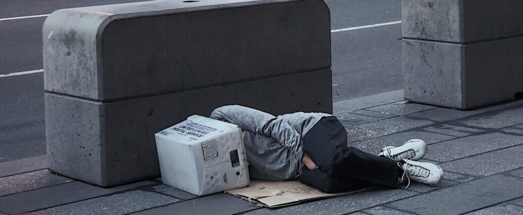 This image shows someone lying down on the floor next to what could be described as hostile architecture, because the seating area is small and has no back rest.