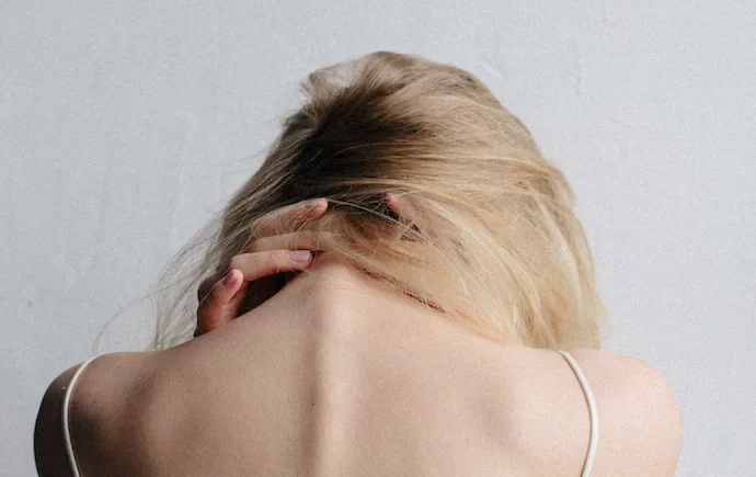 A young white woman in blonde hair gripping her neck in distress.