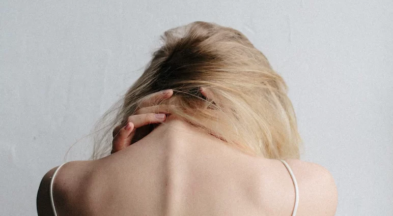 A young white woman in blonde hair gripping her neck in distress.