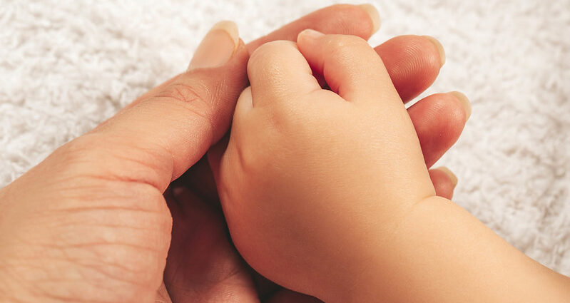 A newborn baby's hand rests on the palm of its mother.