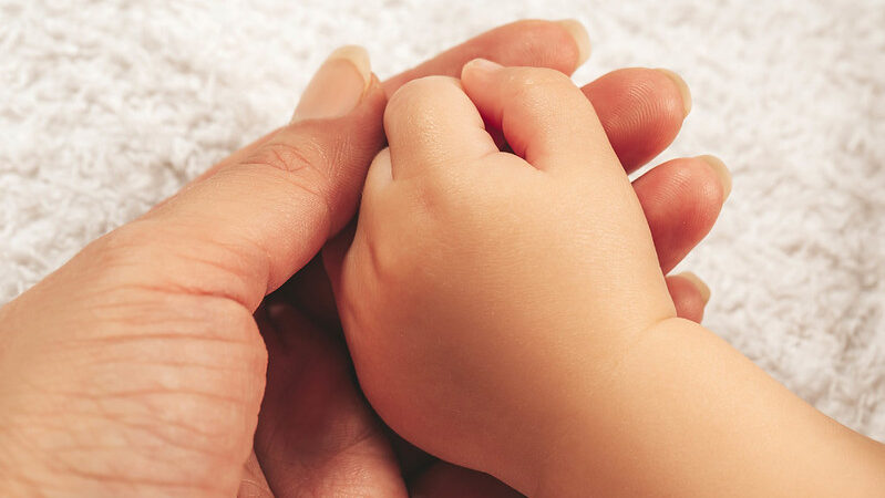 A newborn baby's hand rests on the palm of its mother.