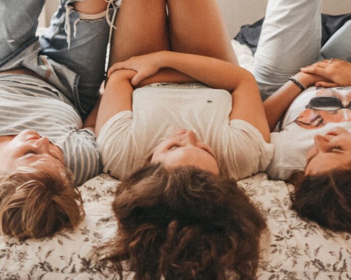 Image shows three teenage girls lying on a bed side-by-side.