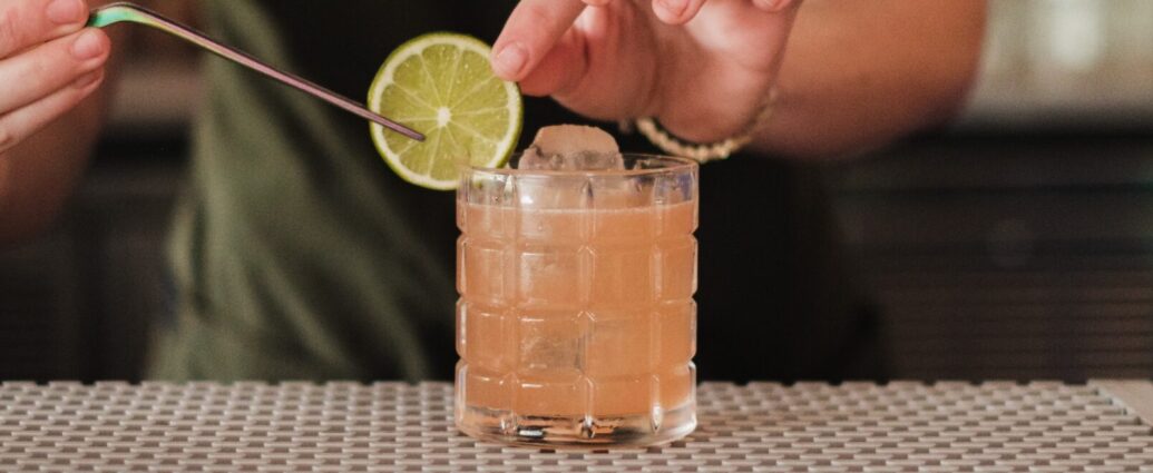 Image shows a bartender placing a lime on the rim of a non-alcoholic cocktail