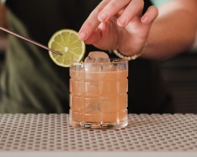 Image shows a bartender placing a lime on the rim of a non-alcoholic cocktail