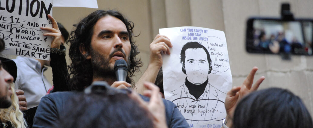 Image shows Russell Brand speaking at a protest on Wall Street, NYC.