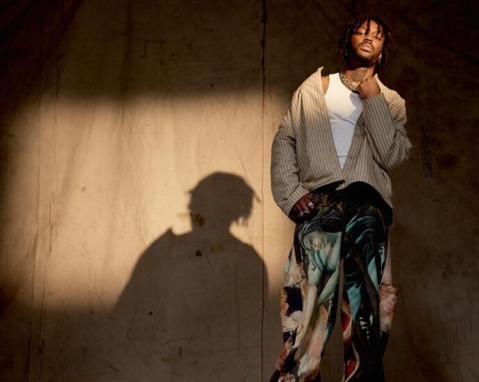 Singer VJ Jaxson stands onstage with a curtain and a shadow behind him.