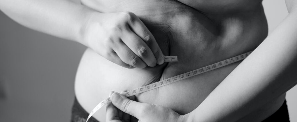 Grayscale photo of woman wrapping measuring tape around her stomach.