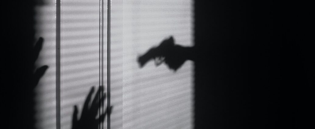 Image shows a shadow silhouette of an arm holding a gun.