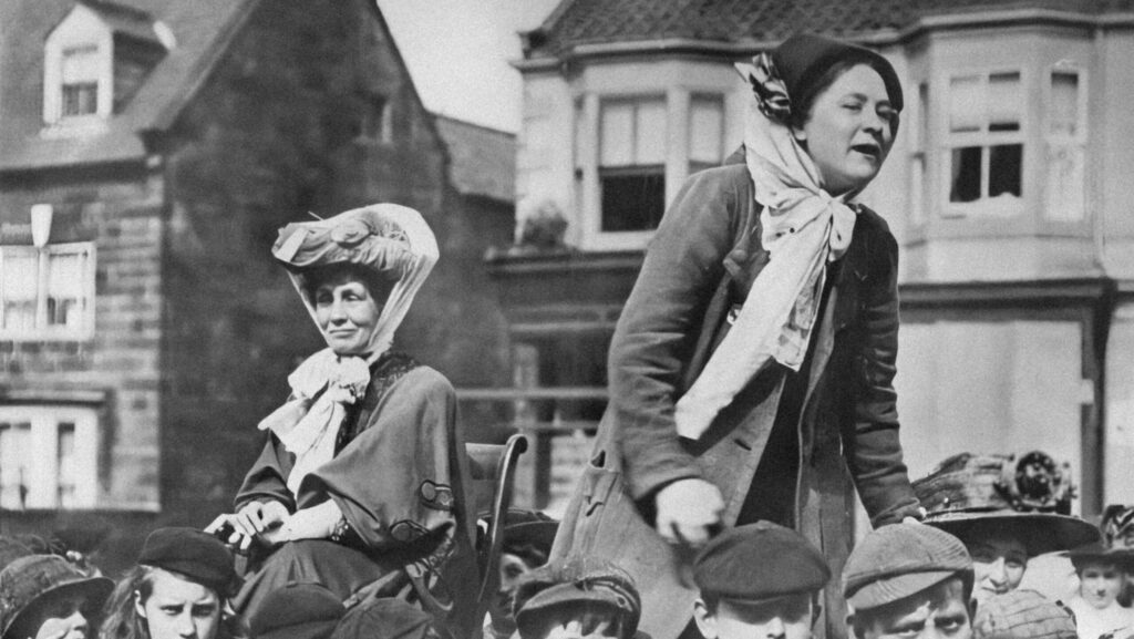 Two suffragettes standing on a cart, bringing their message. England, location unknown, about 1900.