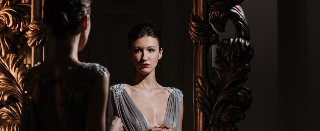 Brunette woman dressed in silver dress looking in mirror.