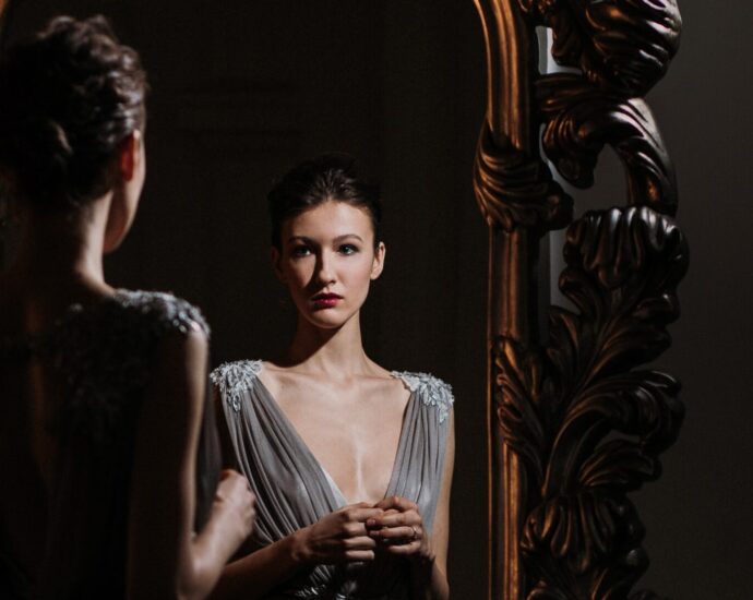 Brunette woman dressed in silver dress looking in mirror.