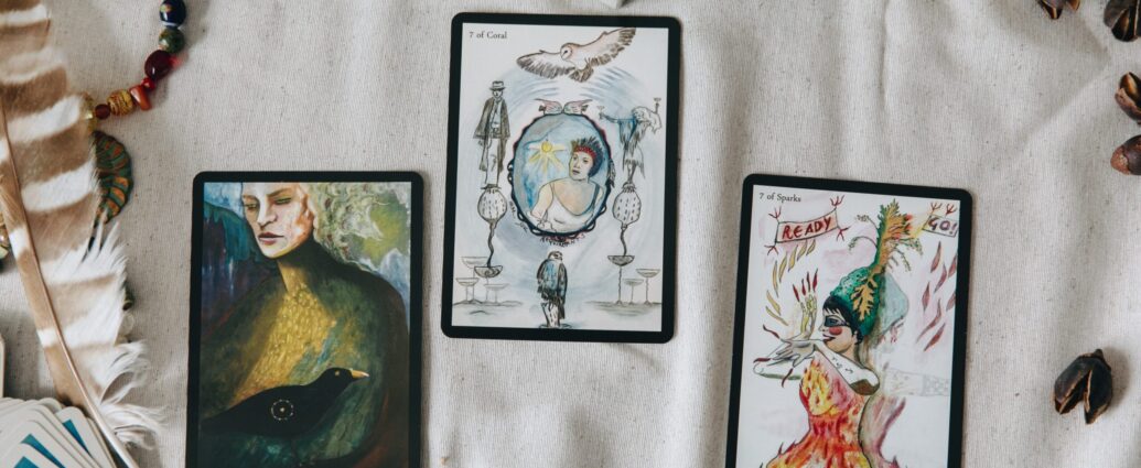 Image shows three tarot cards facing upwards on a table, surrounded by feathers and beads [Why do men hate astrology?]