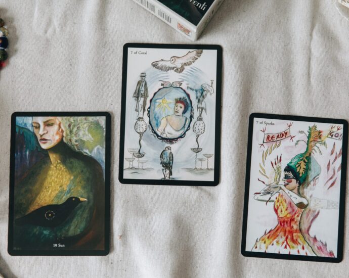 Image shows three tarot cards facing upwards on a table, surrounded by feathers and beads [Why do men hate astrology?]