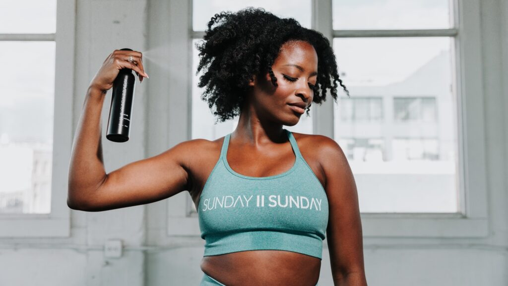 A Black woman misting her curly hair with product.