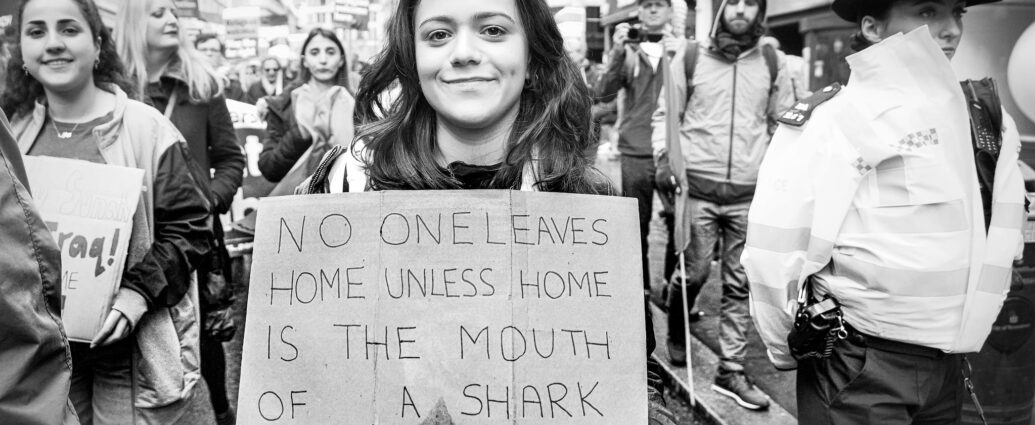 Image taken during the March Against Racism in central London on Saturday on 18 March. A protestor holds a sign reading 'No One Leaves Home Unless Home Is The Mouth Of A Shark'.