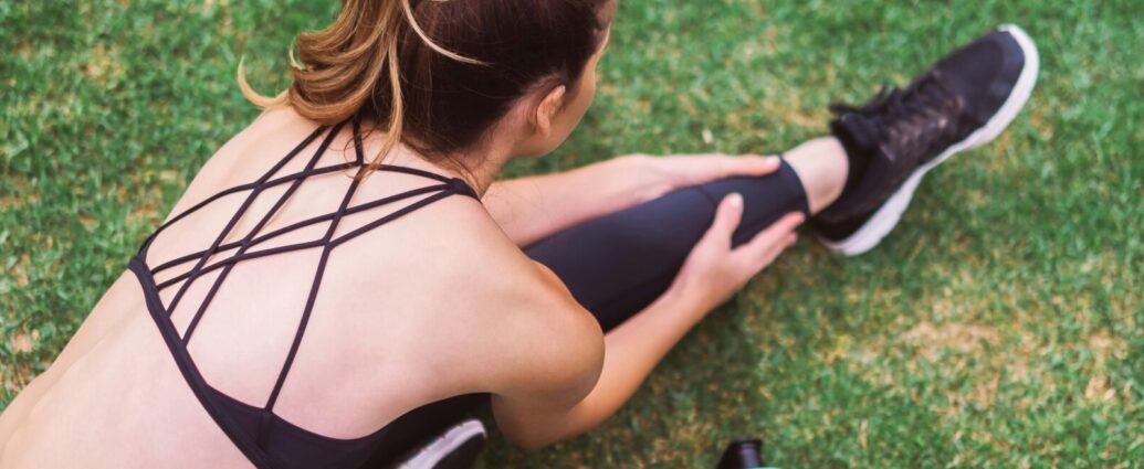 Image shows a women wearing black athleisure, stretching on the grass.