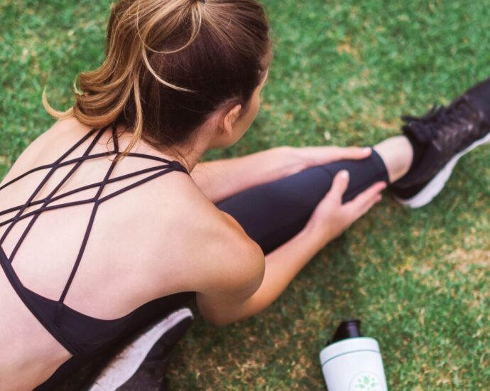 Image shows a women wearing black athleisure, stretching on the grass.