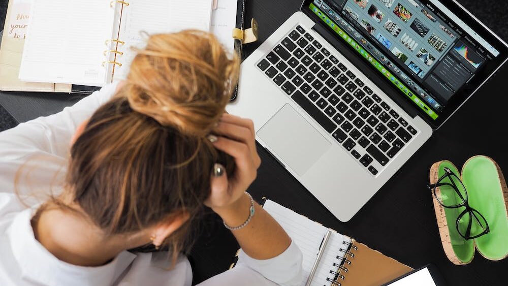 Woman with her head down sitting at laptop with writers block.