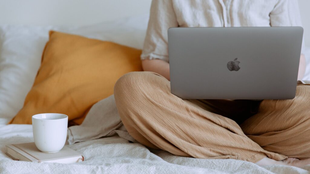 person sitting crossed legged on a bed with a laptop in their lap. My journalism journey.