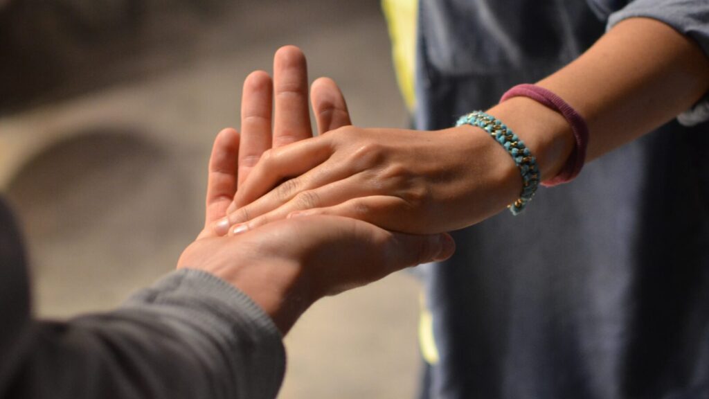 Image shows a hand reaching out to hold another hand. Help a friend with trauma.