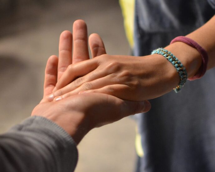 Image shows a hand reaching out to hold another hand. Help a friend with trauma.