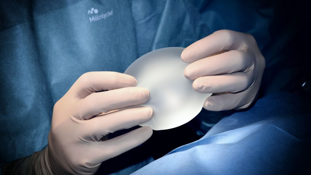 Image shows hands wearing surgical gloves holding a silicone breast implant.