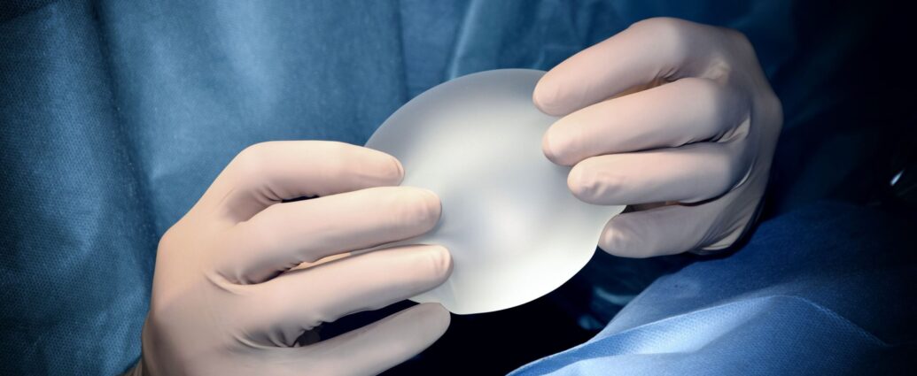 Image shows hands wearing surgical gloves holding a silicone breast implant.