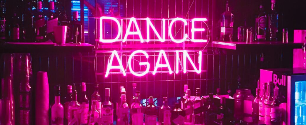 Neon light sign reading DANCE AGAIN in a bar.