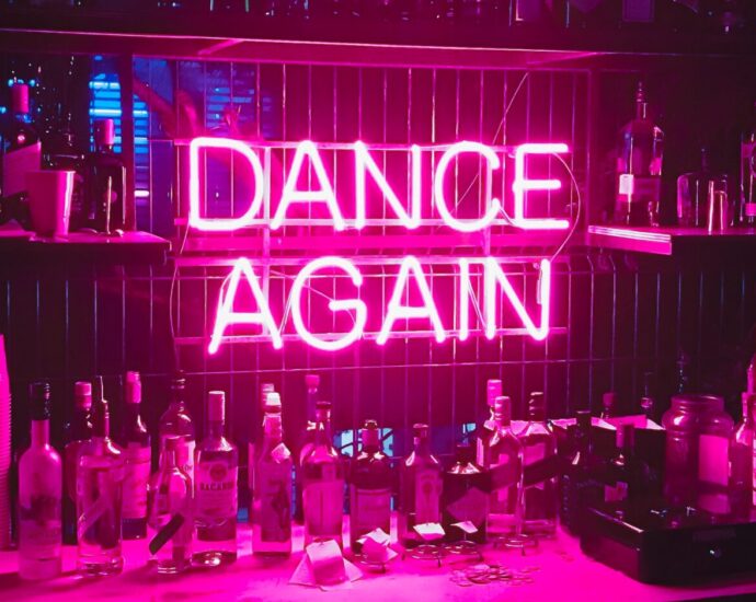 Neon light sign reading DANCE AGAIN in a bar.