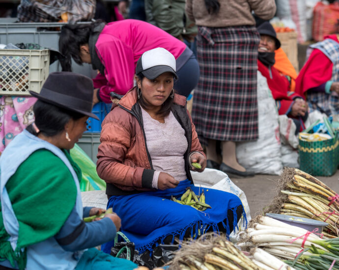 Two women sat behind a pile of vegetables on a busy market street in Ecuador.