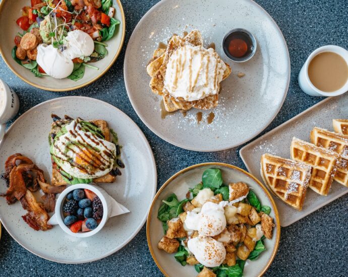 A table of brunch dishes including eggs on toast, bacon, berries and waffles.