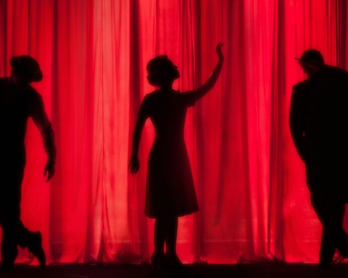 Three silhouettes standing in front of a red stage curtain.