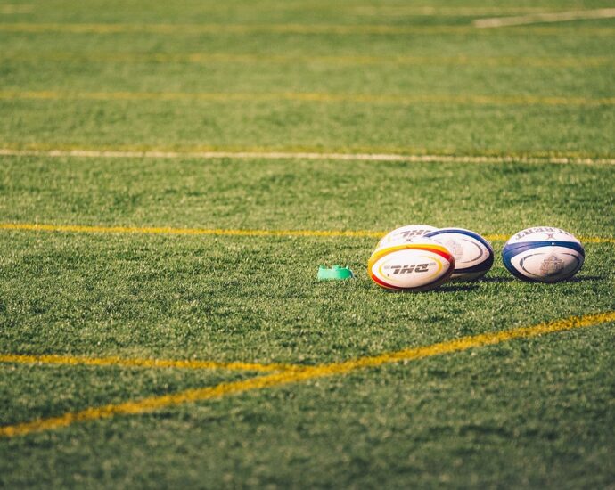 Image shows three rugby balls on a pitch.